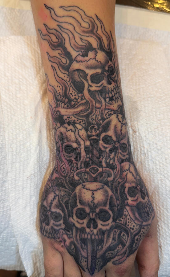 Black and gray skulls and sword hand tattoo Black and gray style tattoo ofskulls with a sword on clients hand